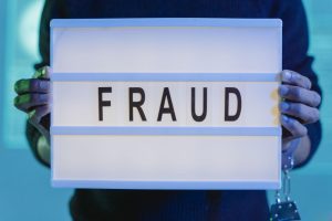 A person holding a lightbox with the word ‘FRAUD’ in capital letters