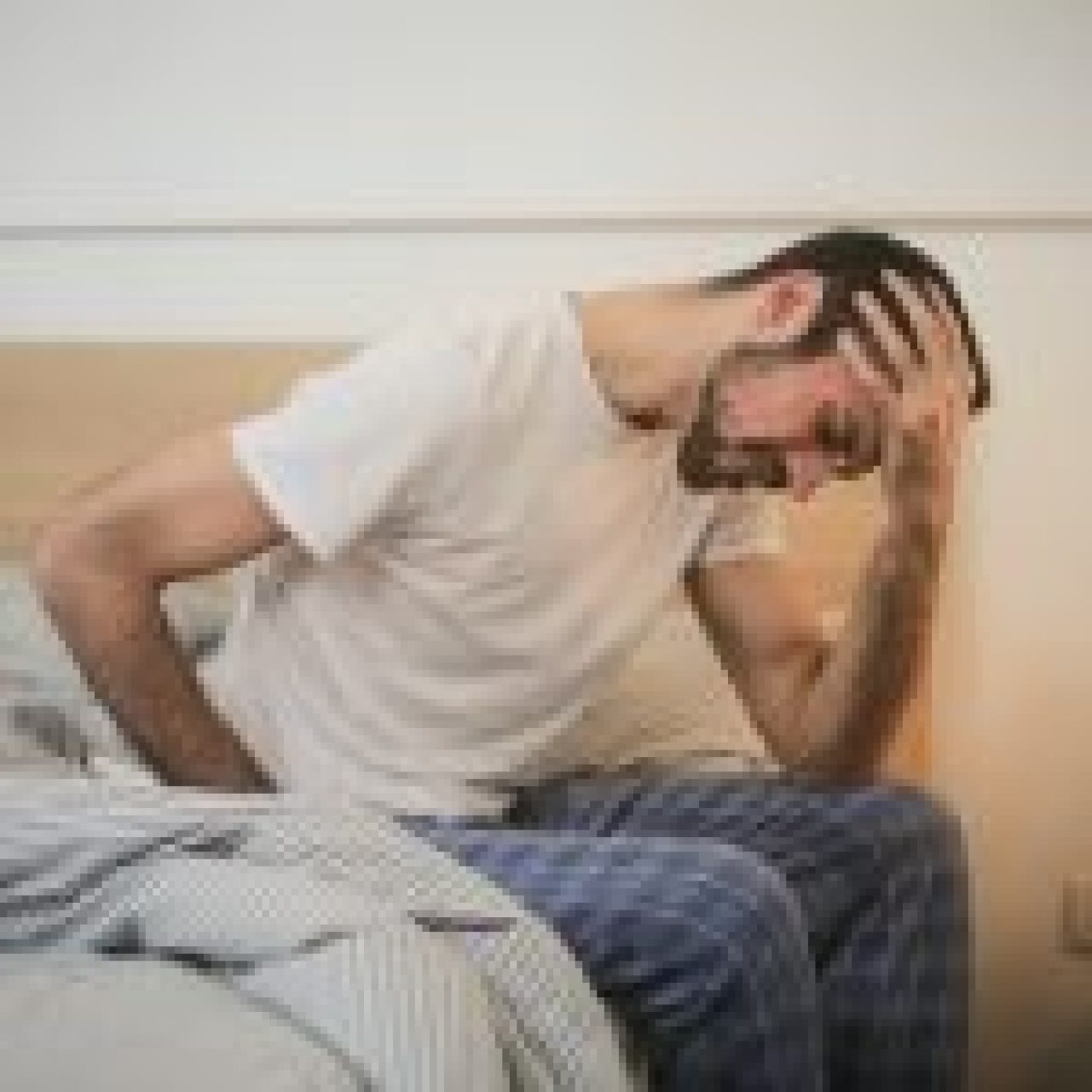 Person in distress sitting on bed holding head, depicting discomfort possibly related to sciatic nerve pain.
