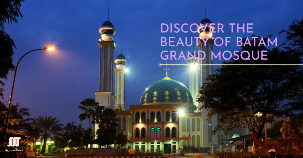 A twilight view of the Batam Grand Mosque with illuminated minarets and a green and blue dome, surrounded by trees under a dusky sky. The image has text that reads “DISCOVER THE BEAUTY OF BATAM GRAND MOSQUE” in bold white letters.
