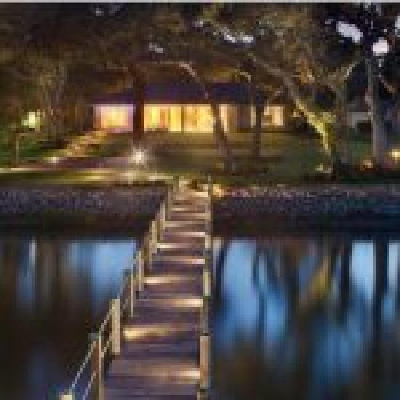 Twilight view of a tranquil waterfront property illuminated by solar dock lights along a wooden dock leading to an inviting house. #Solar dock lights