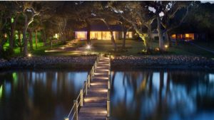Twilight view of a tranquil waterfront property illuminated by solar dock lights along a wooden dock leading to an inviting house. #Solar dock lights
