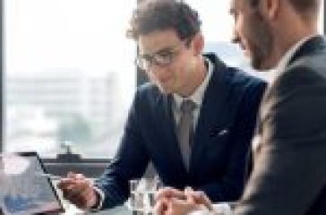 Two professionals in a business meeting, with one showing data graphs on a laptop screen, highlighting the importance of professional services.