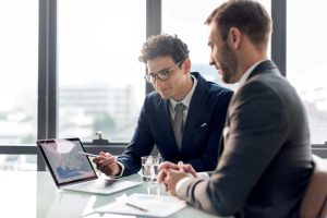 Two professionals in a business meeting, with one showing data graphs on a laptop screen, highlighting the importance of professional services.