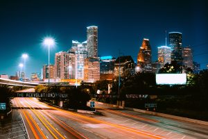Nighttime view of Houston’s illuminated skyline with light trails from vehicles on a highway.