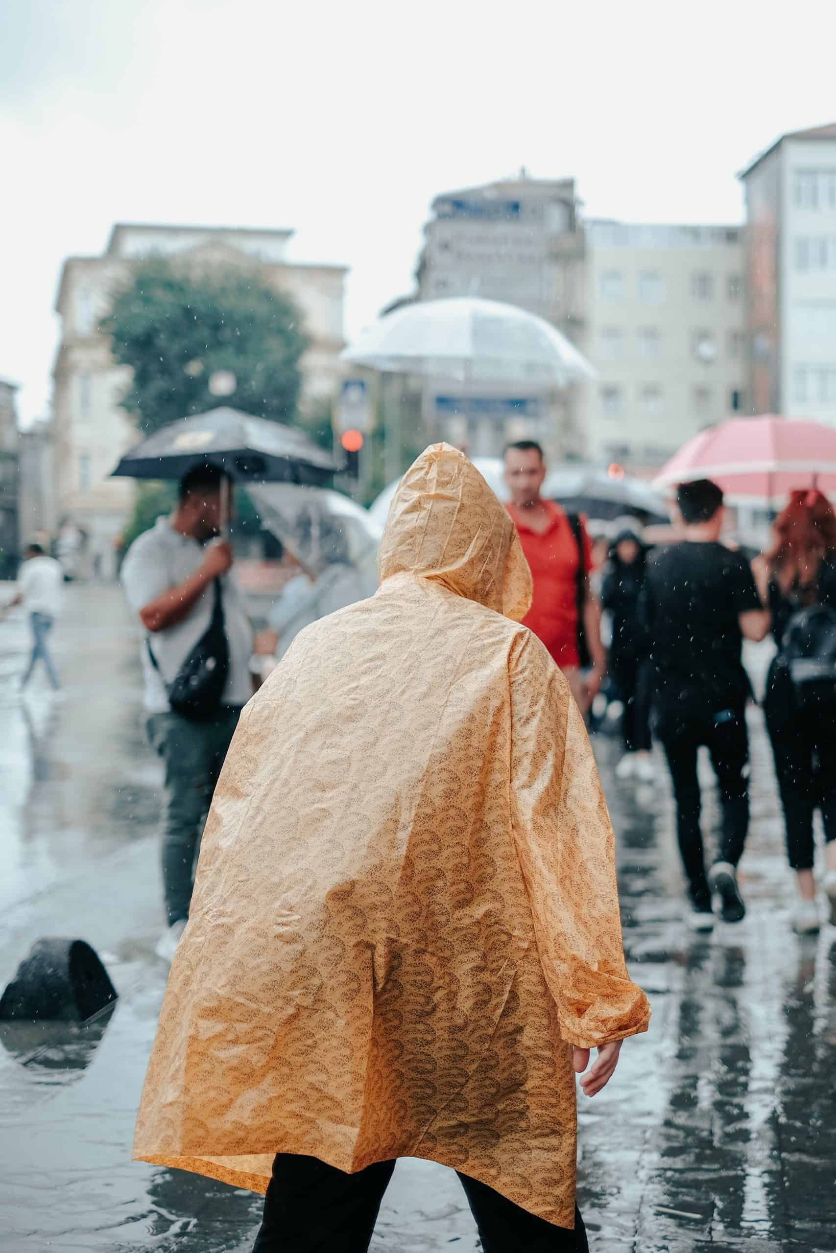 Moderate Rainfall Warning: A person in a yellow raincoat walking on a wet street with other pedestrians carrying umbrellas in the background.