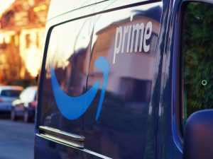 Close-up view of an Amazon Prime logo on a vehicle’s window against a blurred urban backdrop.