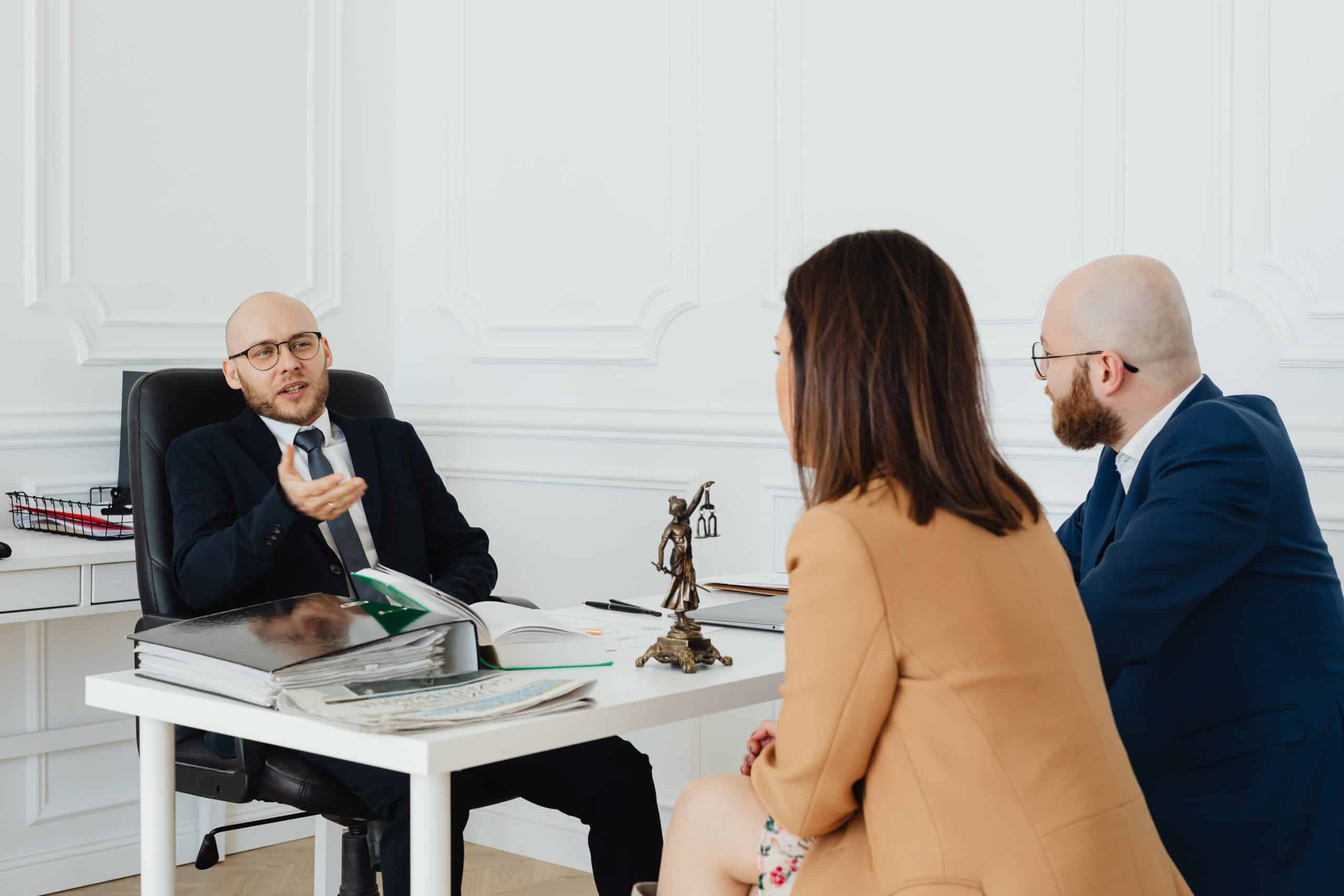 Three professionals discussing legal matters in an office setting with documents on the desk.