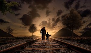 Silhouette of an adult holding a child’s hand on railway tracks leading towards mountains at sunset. #Balancing Screen Time