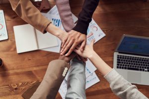 Team members joining hands over a worktable filled with business strategy documents and a laptop, symbolizing collaboration in SEO efforts.