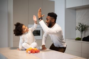Two people high-fiving over a kitchen counter with a bowl of oranges in front #Vitamin E