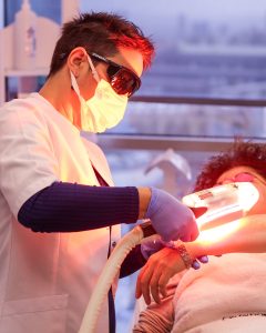 Laser Hair Removal :A professional in a white coat and protective eyewear administers a laser skin treatment to a client lying down, wearing protective goggles.