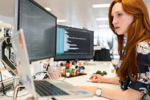 A woman working on a computer with multiple monitors displaying code and data. #Accurate Data Labeling