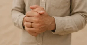 Wedding Band Choice and Businesses 3 Man's hands clasped wearing thin gold wedding band in beige shirt sleeves against soft sandy background