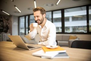 Person in a white shirt drinking coffee while working on a laptop in a modern office setting. #high-paying jobs