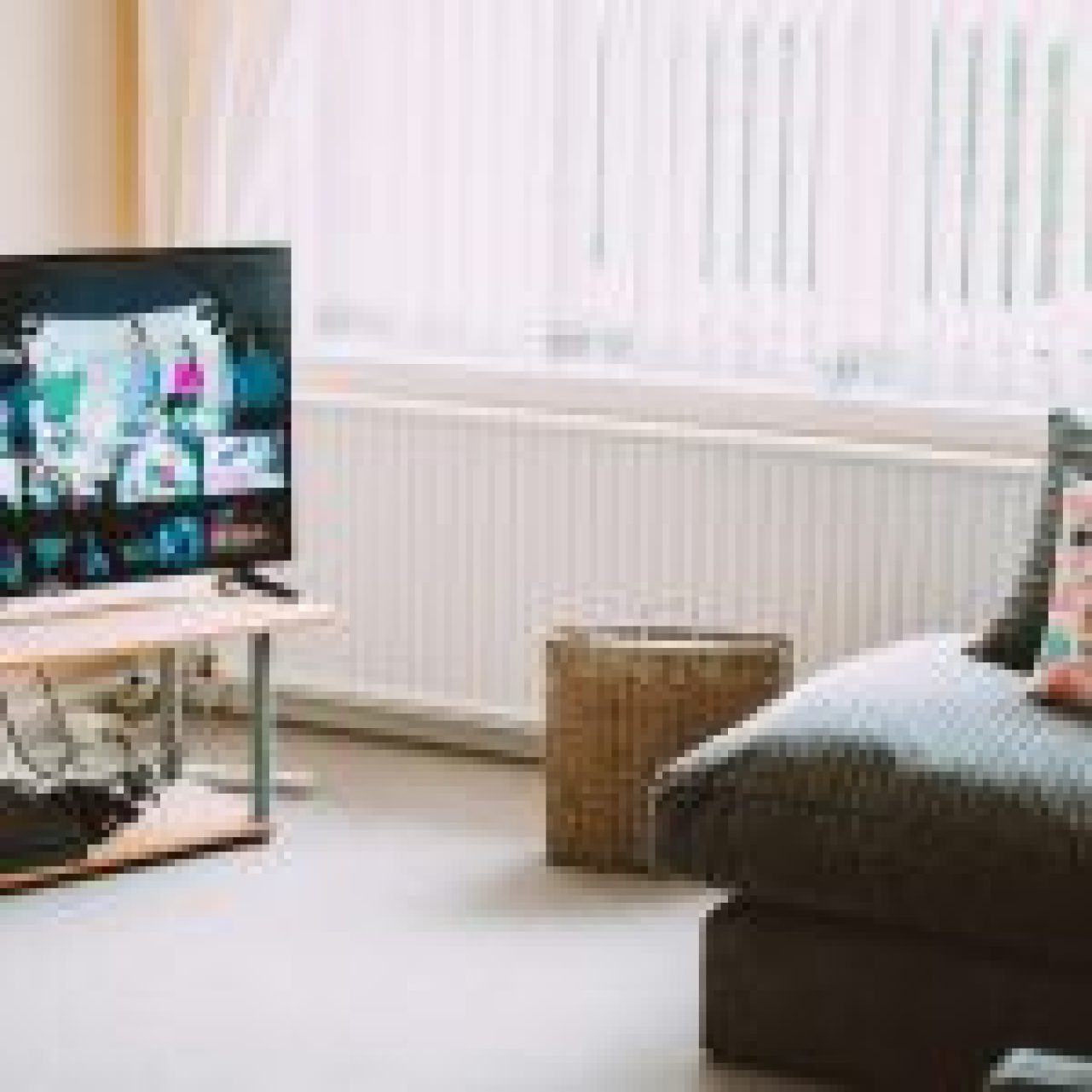 A cozy living room with a TV displaying a streaming service interface, a grey couch with colourful pillows, and a wicker basket on the floor.