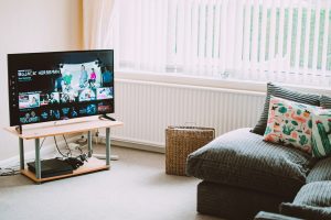 A cozy living room with a TV displaying a streaming service interface, a grey couch with colourful pillows, and a wicker basket on the floor.