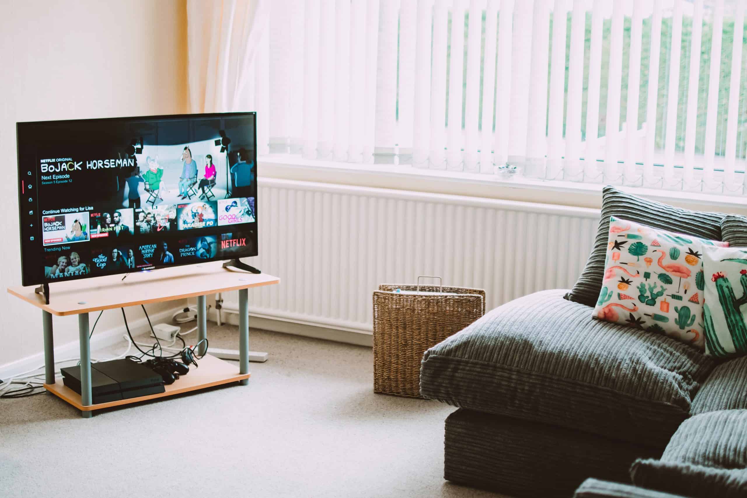 A cozy living room with a TV displaying a streaming service interface, a grey couch with colourful pillows, and a wicker basket on the floor.
