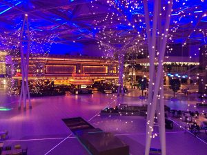 Indoor area with vibrant purple and blue lighting, featuring hanging lights creating a starry effect, with 'The Cheesecake Factory' in the background.