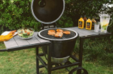 Outdoor barbecue grill with chicken, salad, sauces, and lemonade.