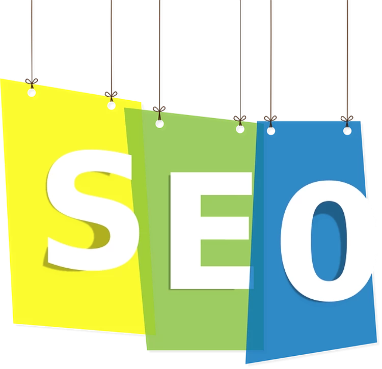 Three hanging signs with the letters ‘S’, ‘E’, and ‘O’ on them, respectively, in a staggered arrangement. The signs are colored yellow, green, and blue from left to right. The background is white and the overall image suggests a focus on SEO, which stands for Search Engine Optimization.