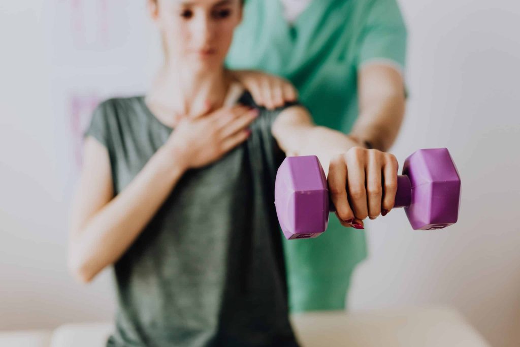 A person performing a bicep curl with a purple dumbbell while being assisted by another individual.