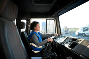A truck drivers wearing a safety helmet and reflective vest, standing next to a large truck on a New York road.