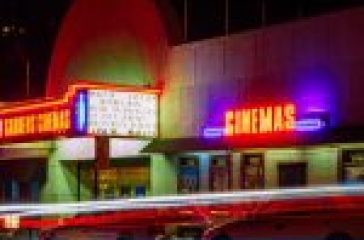 Neon-lit cinema marquee at night with colorful light trails from moving traffic. #Moviesflix