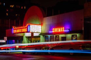 Neon-lit cinema marquee at night with colorful light trails from moving traffic. #Moviesflix