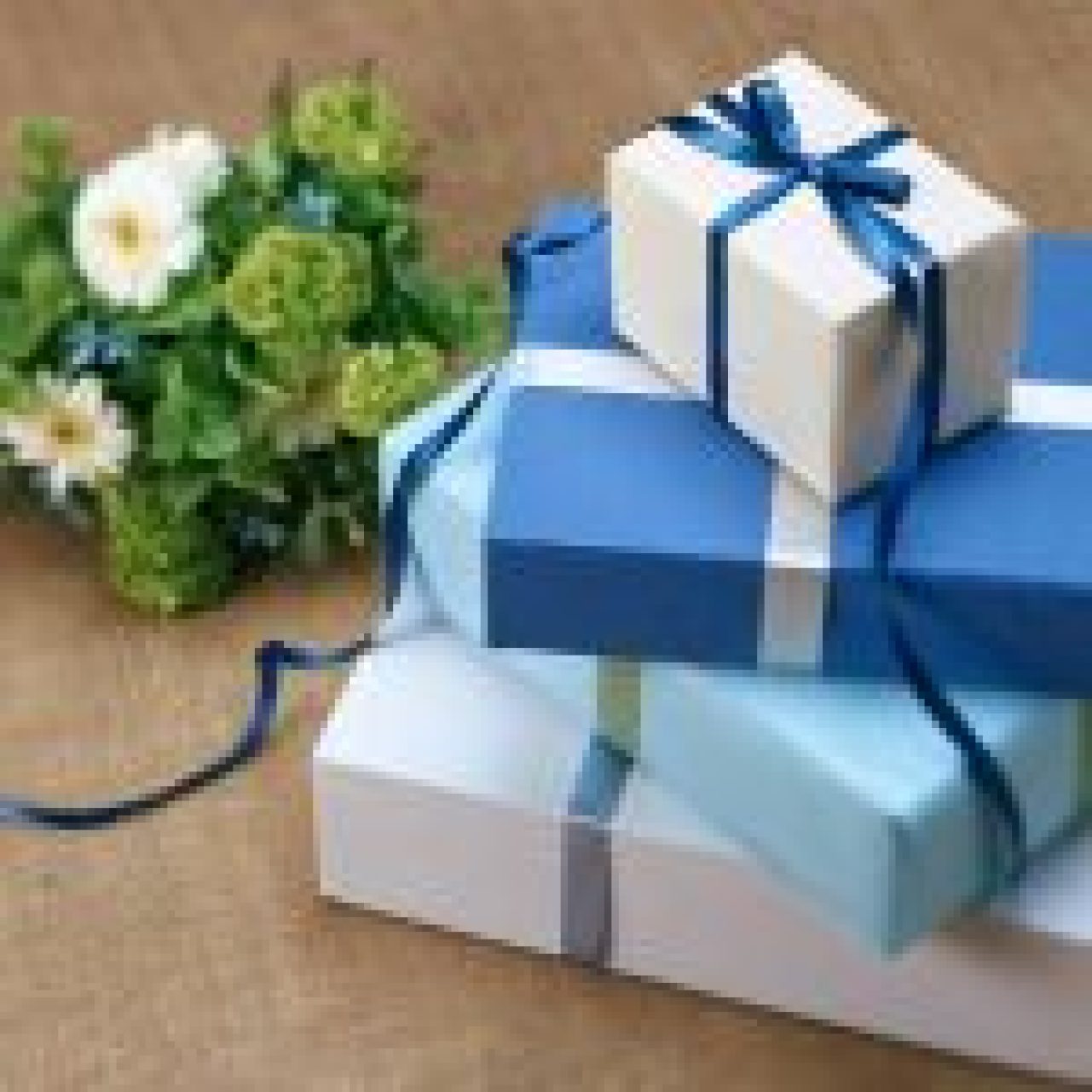 Stacked blue and white gift boxes with ribbon next to a bouquet of flowers on textured background.