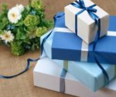 Stacked blue and white gift boxes with ribbon next to a bouquet of flowers on textured background.