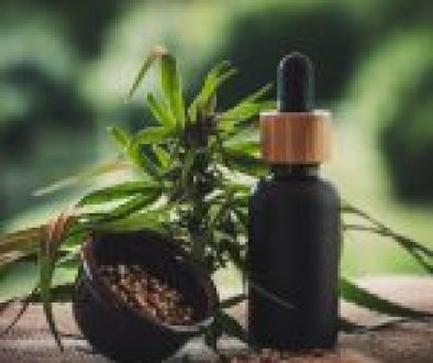 A dropper bottle of medicinal cannabis oil beside hemp seeds and a fresh cannabis plant on a wooden surface. #Medicinal Cannabis Clinics