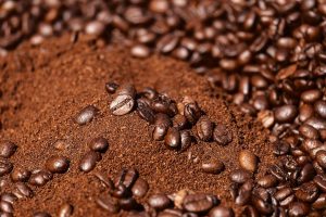 Close-up of freshly ground coffee surrounded by whole roasted beans, representing the process of flavoring coffee.