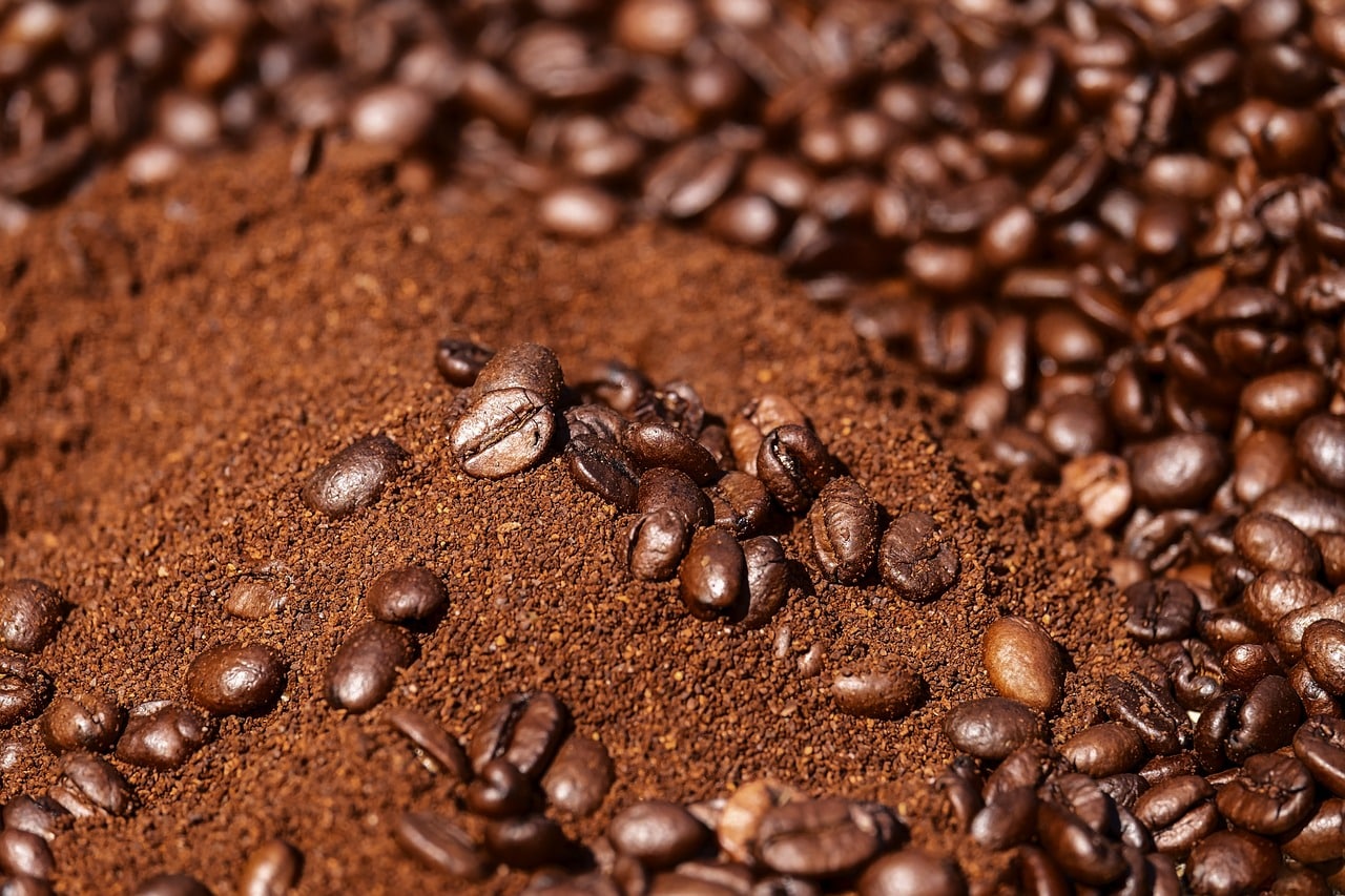 Close-up of freshly ground coffee surrounded by whole roasted beans, representing the process of flavoring coffee.