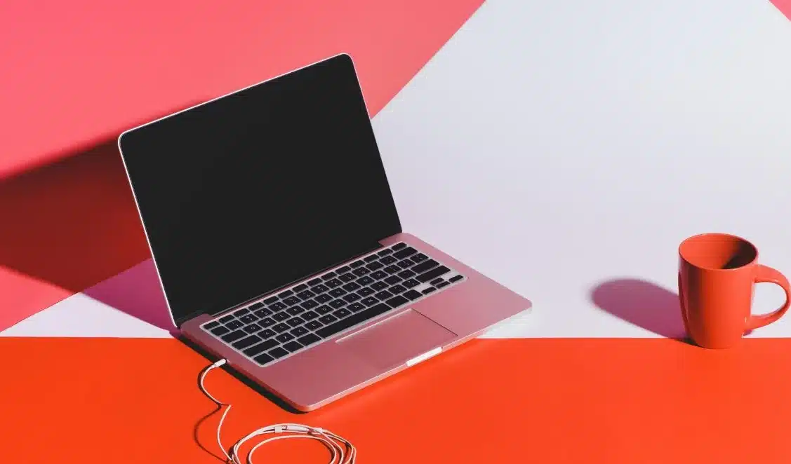 A laptop with a black screen and a red coffee mug on a red and white surface.