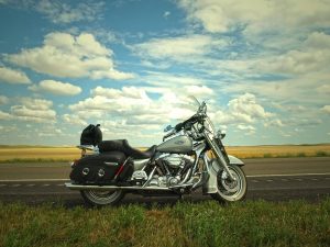 A parked motorcycle on an open road beside a grassy field under a vast sky, symbolizing freedom and the importance of rider safety.