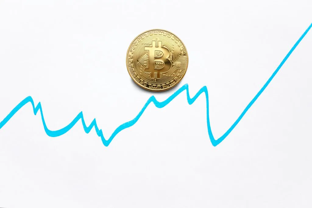 A physical Bitcoin token is centered on a white background, with a fluctuating blue line graph behind it, suggesting the concept of cryptocurrency value changes or market volatility. #Blockchain in Banking