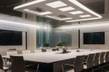 Modern conference room with a large white table and chairs, glass walls, recessed lighting, and dual monitors.
