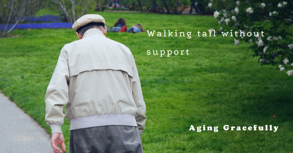 An elderly person walking in a park, wearing a hat and light-colored jacket, with people sitting on the grass and trees with white blossoms in the background. Text on the image reads ‘Walking tall without support’ and ‘Aging Gracefully’