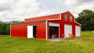 A red metal farm building with white doors set against a backdrop of lush greenery and overcast skies, exemplifying modern agricultural infrastructure.