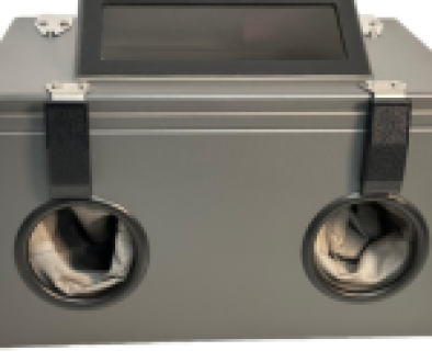 A gray sandblasting cabinet with a viewing window and two gloved armholes