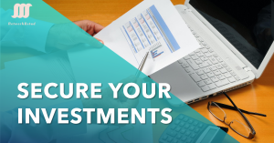 A person holding a document with charts and graphs, pointing at it with a pen, next to an open laptop, calculator, and glasses on a wooden desk. The text "SECURE YOUR INVESTMENTS" is prominently displayed in bold white letters on a teal overlay. The logo and name "NetworkUstad" are visible in the top left corner.