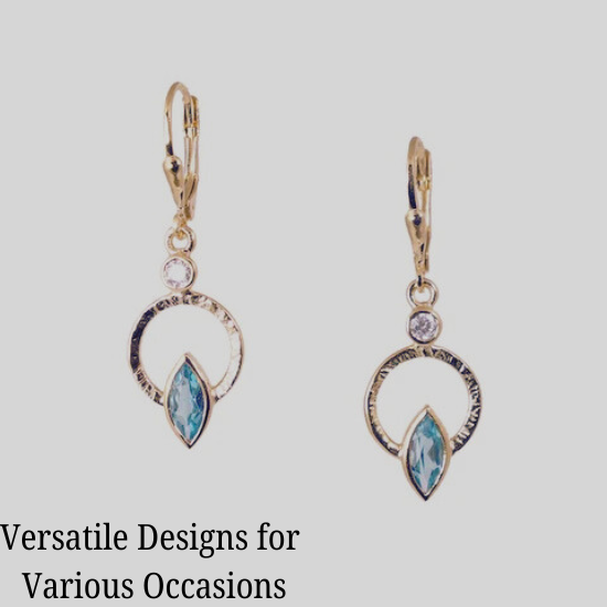 A pair of gold earrings with a circular design, featuring a small clear gemstone at the top and a larger blue marquise-shaped gemstone at the bottom. The earrings are displayed against a light background.