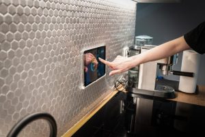 A person is interacting with a touchscreen embedded in a kitchen backsplash.