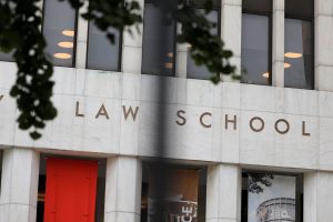 The exterior facade of a law school building with large windows and signage on a marble surface.