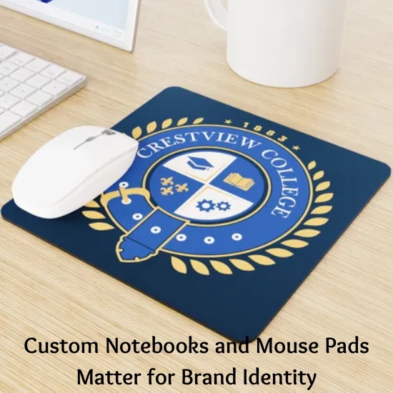 A custom mouse pad with the Crestview College logo on a desk, accompanied by a white mouse, a keyboard, and a coffee mug. The text below reads, "Custom Notebooks and Mouse Pads Matter for Brand Identity."