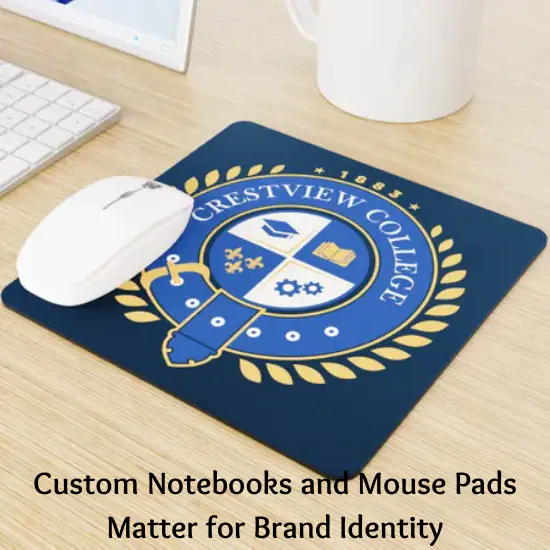 A custom mouse pad with the Crestview College logo on a desk, accompanied by a white mouse, a keyboard, and a coffee mug. The text below reads, "Custom Notebooks and Mouse Pads Matter for Brand Identity."