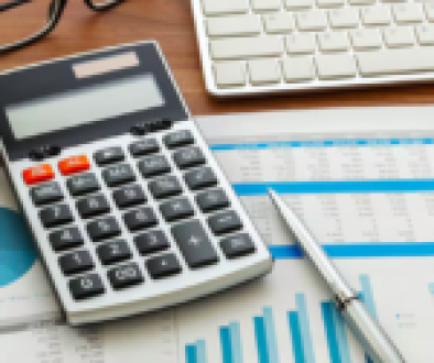 A calculator, financial documents with graphs and charts, a pen, and a keyboard on a desk.