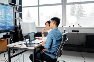 Two software engineers collaborating on code while working on multiple monitors in a modern office space.