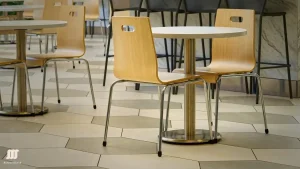 A modern restaurant with small round tables and wooden chairs on a hexagonal tiled floor, featuring a counter in the background.