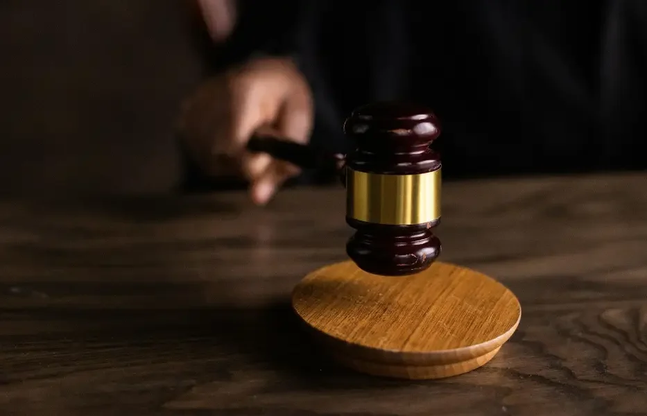 A wooden gavel resting on its sounding block, held by a hand in a judicial robe, symbolizing legal authority.